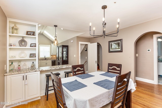 dining area featuring light wood-style flooring, arched walkways, an inviting chandelier, baseboards, and vaulted ceiling