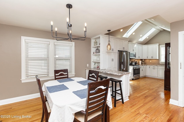 dining area featuring light wood-type flooring, lofted ceiling with skylight, baseboards, and a chandelier