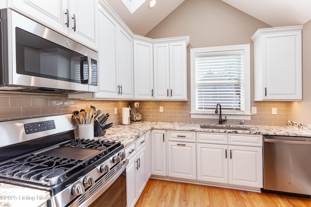 kitchen featuring vaulted ceiling, light wood-style floors, white cabinets, stainless steel appliances, and a sink