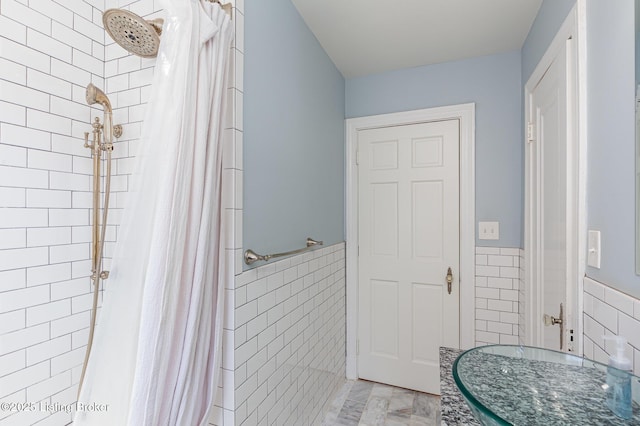 full bath featuring a wainscoted wall, tile walls, and tiled shower