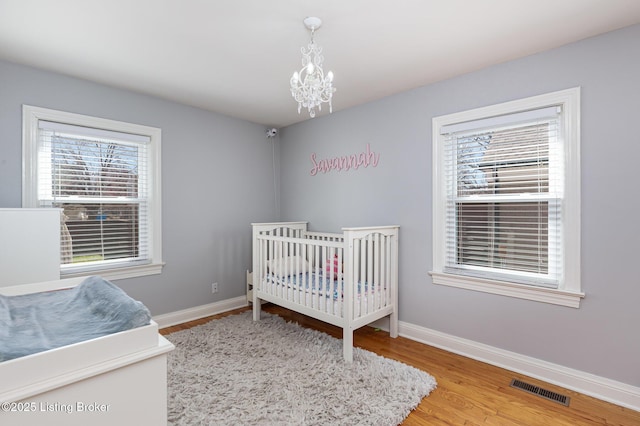 bedroom with a chandelier, visible vents, baseboards, and wood finished floors