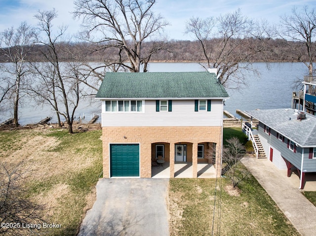 view of front facade with stairway, a water view, driveway, and a shingled roof