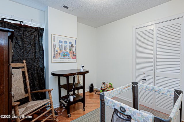 bedroom with visible vents, a textured ceiling, wood finished floors, a closet, and baseboards