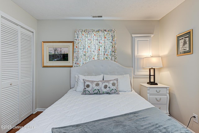 bedroom featuring visible vents, baseboards, wood finished floors, a closet, and a textured ceiling