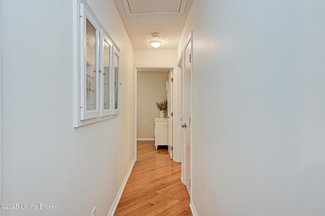 corridor with baseboards, a textured ceiling, and light wood finished floors