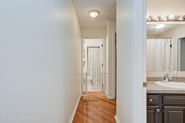 hallway with a textured ceiling, baseboards, light wood finished floors, and a sink