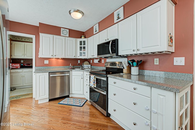 kitchen featuring white cabinets, light wood-style flooring, appliances with stainless steel finishes, and a textured ceiling