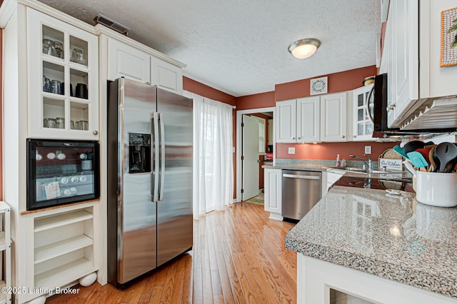 kitchen with light wood-style flooring, a textured ceiling, stainless steel appliances, white cabinets, and glass insert cabinets