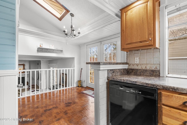 kitchen featuring tasteful backsplash, dark countertops, vaulted ceiling with skylight, an inviting chandelier, and dishwasher