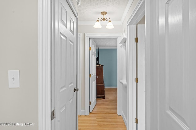 hall featuring crown molding, baseboards, a chandelier, light wood-style flooring, and a textured ceiling