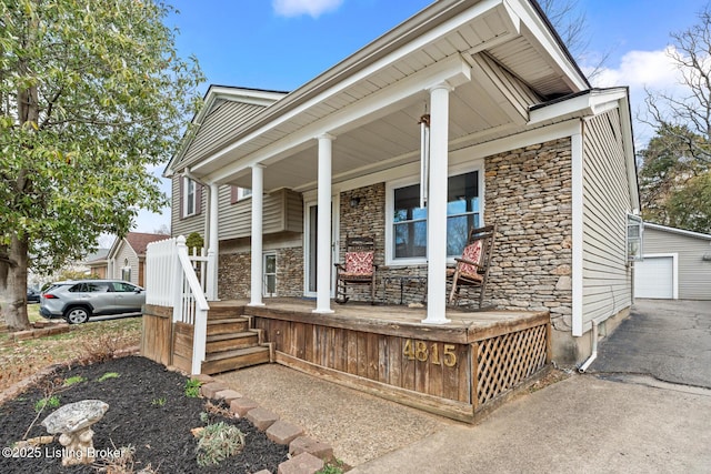 view of front of house with an outbuilding, driveway, stone siding, a detached garage, and a porch