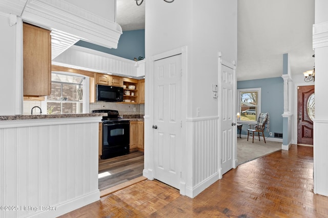 kitchen with visible vents, black appliances, a towering ceiling, wainscoting, and tasteful backsplash