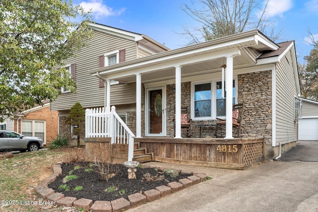 view of front of property featuring a porch, stone siding, and a detached garage