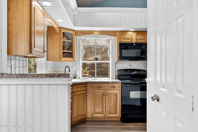 kitchen with black appliances, a sink, tasteful backsplash, wood finished floors, and glass insert cabinets