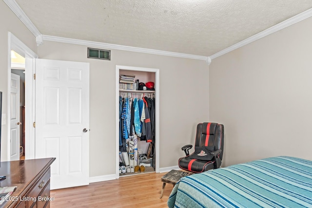 bedroom featuring visible vents, ornamental molding, light wood-style floors, a closet, and a textured ceiling