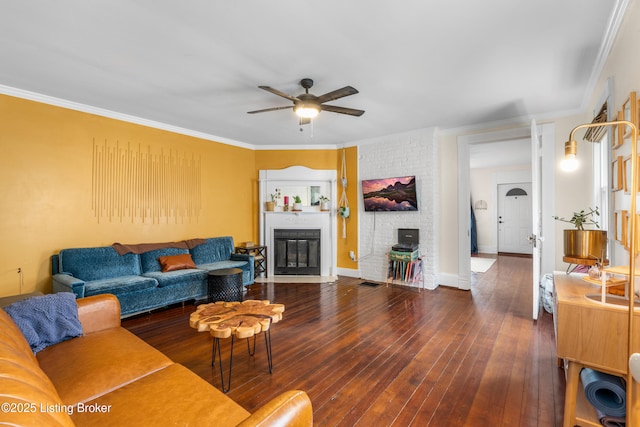 living room with a fireplace with flush hearth, dark wood-type flooring, ornamental molding, a ceiling fan, and baseboards