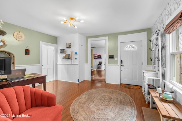 foyer with an inviting chandelier, wood finished floors, and a wainscoted wall