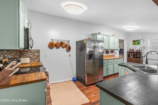 kitchen featuring a sink, green cabinetry, butcher block countertops, and stainless steel fridge with ice dispenser