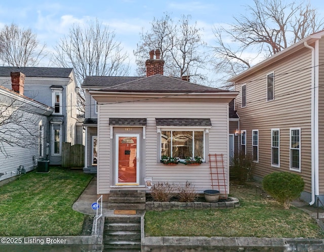 view of front of home with central AC unit, entry steps, a chimney, and a front lawn