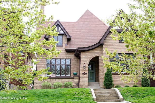 tudor-style house featuring a front lawn and brick siding