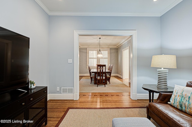 living area featuring visible vents, crown molding, baseboards, an inviting chandelier, and wood finished floors