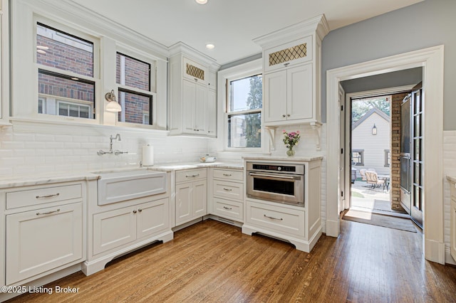 kitchen with light stone countertops, stainless steel oven, decorative backsplash, light wood-style floors, and a sink