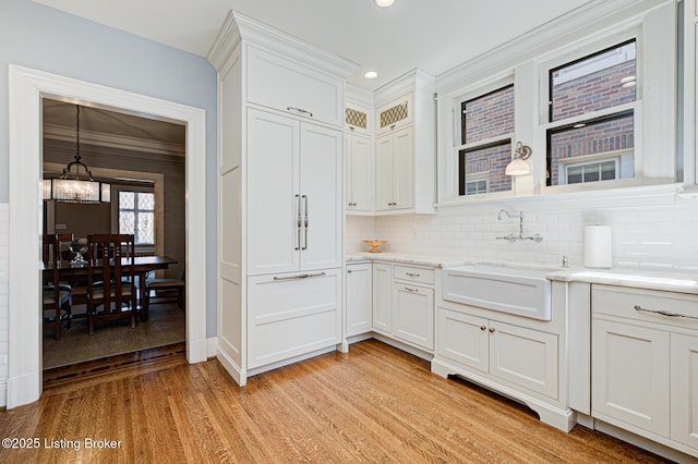 kitchen with a sink, white cabinetry, light wood-style floors, an inviting chandelier, and decorative backsplash