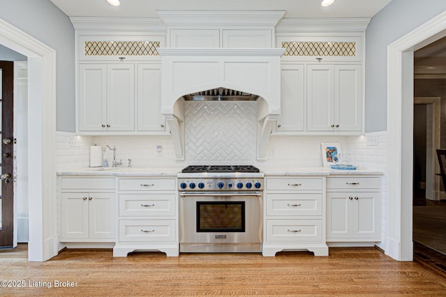 kitchen featuring white cabinetry, a sink, decorative backsplash, light wood-style floors, and high end stainless steel range oven