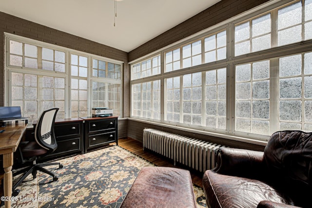 home office featuring wood finished floors, brick wall, and radiator heating unit