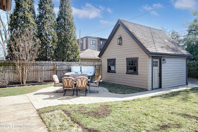 rear view of house with a shingled roof, fence, a lawn, an outdoor structure, and a patio