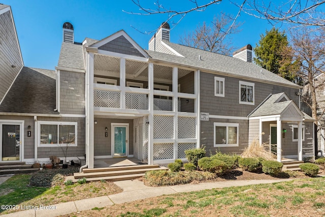 view of property featuring a porch, a balcony, roof with shingles, and a chimney