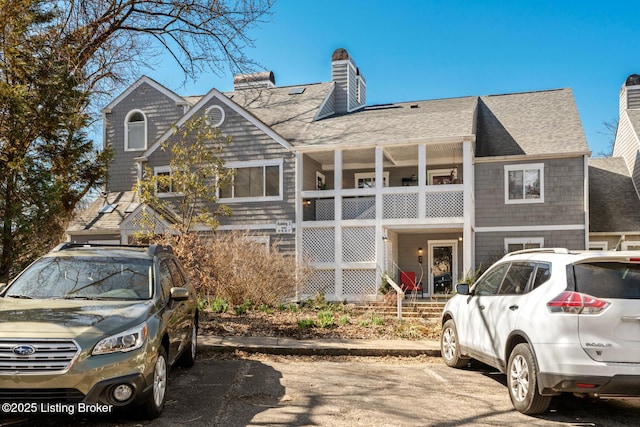 shingle-style home with a shingled roof, a balcony, and a chimney