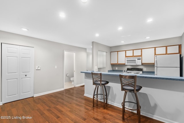 kitchen featuring a kitchen breakfast bar, dark wood finished floors, recessed lighting, white appliances, and baseboards