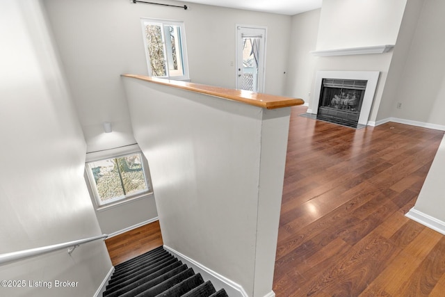 stairway featuring baseboards, a fireplace with flush hearth, and wood finished floors