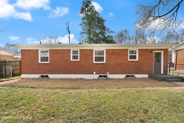 rear view of house featuring a lawn, brick siding, and fence