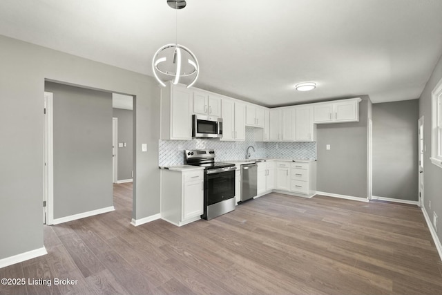 kitchen featuring stainless steel appliances, light countertops, white cabinets, light wood-style floors, and backsplash