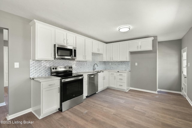 kitchen featuring light wood finished floors, tasteful backsplash, light countertops, appliances with stainless steel finishes, and white cabinetry