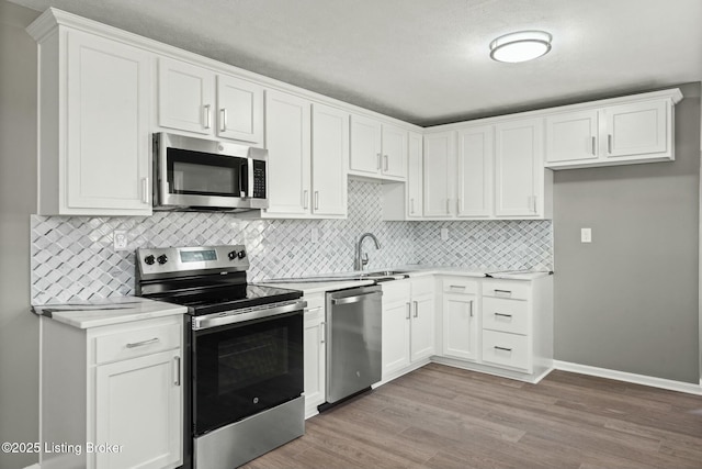 kitchen with a sink, appliances with stainless steel finishes, white cabinets, light wood finished floors, and light countertops