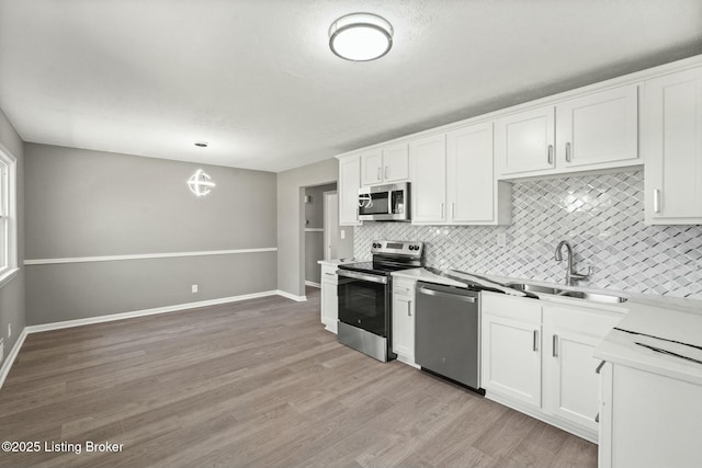 kitchen featuring a sink, stainless steel appliances, light wood-style floors, white cabinetry, and tasteful backsplash