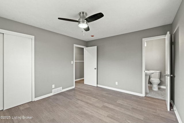 unfurnished bedroom with visible vents, ensuite bath, wood finished floors, baseboards, and ceiling fan