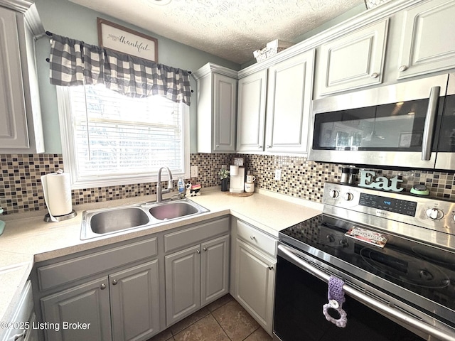 kitchen featuring dark tile patterned flooring, a sink, backsplash, stainless steel appliances, and light countertops