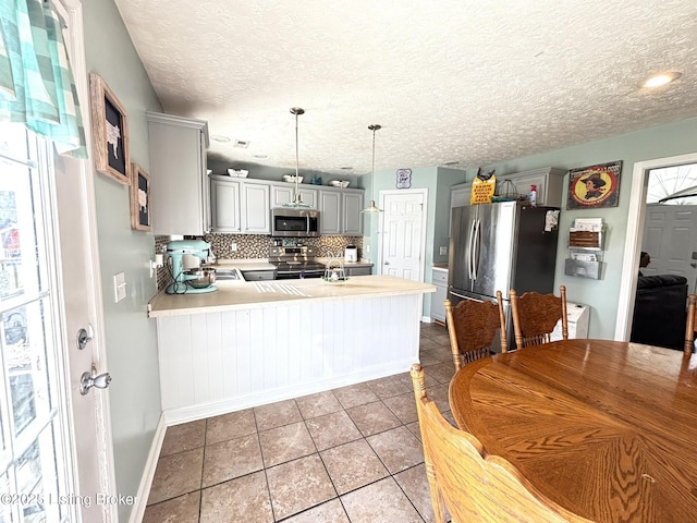 kitchen featuring stainless steel appliances, a peninsula, light tile patterned flooring, light countertops, and decorative backsplash