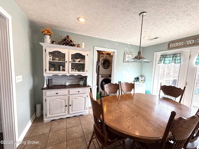 dining room featuring visible vents, baseboards, dark tile patterned floors, a textured ceiling, and stacked washer / drying machine