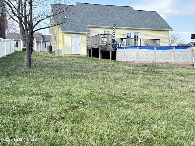 rear view of house featuring fence, a wooden deck, a yard, an outdoor pool, and a shingled roof