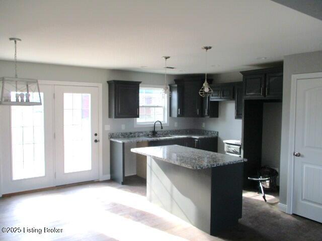 kitchen featuring pendant lighting, stone countertops, a kitchen island, and a sink