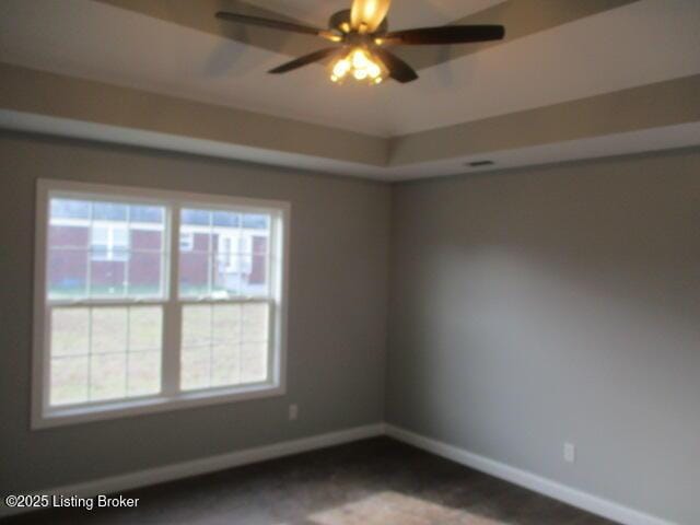 spare room with plenty of natural light, ceiling fan, a tray ceiling, and baseboards