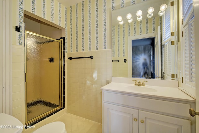 bathroom with wallpapered walls, toilet, wainscoting, a stall shower, and vanity