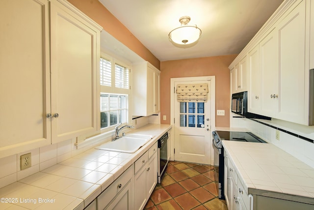 kitchen with dark tile patterned flooring, black appliances, a sink, tasteful backsplash, and tile countertops