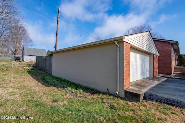 view of side of home featuring a detached garage, fence, aphalt driveway, a lawn, and an outdoor structure