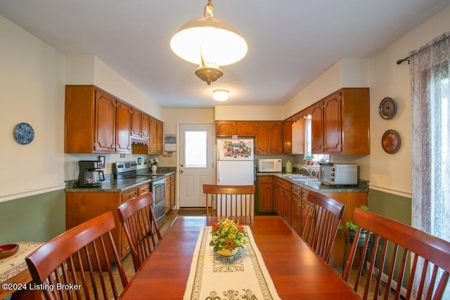 kitchen featuring white appliances, wood finished floors, a sink, dark countertops, and brown cabinets